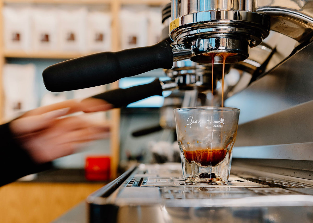 Espresso machine pouring coffee into a glass shot glass on a bar.